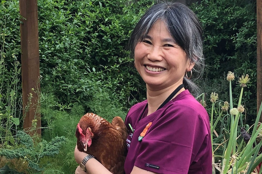 Kim Loo smiles while holding a pet chicken.