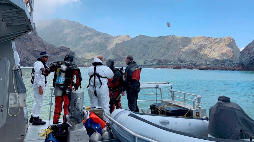 A small group of divers are dressed in protective gear and are preparing to jump into the water from a boat