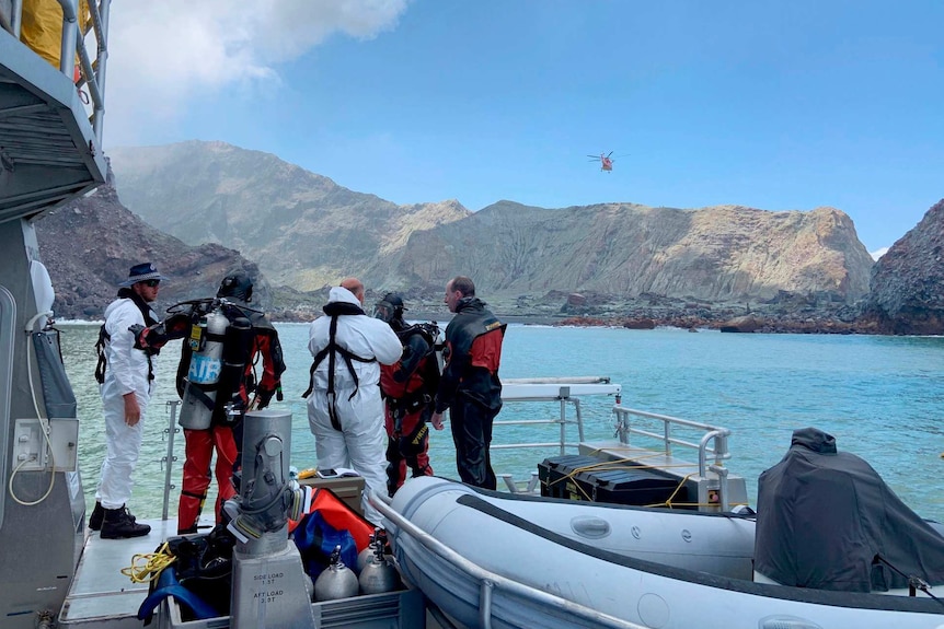 A small group of divers are dressed in protective gear and are preparing to jump into the water from a boat