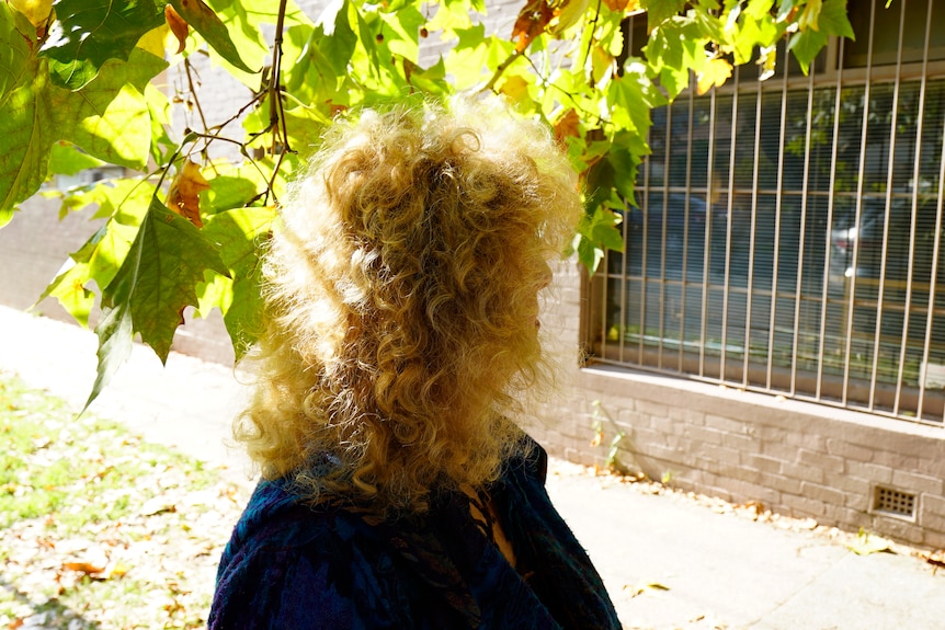 Woman with curly hair looking into the distance, covered by tree branch.