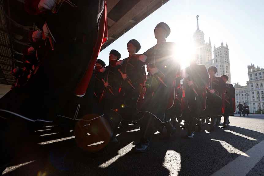 A low-angle image of Russian Cossacks wearing coats and fur hats walking in columns.