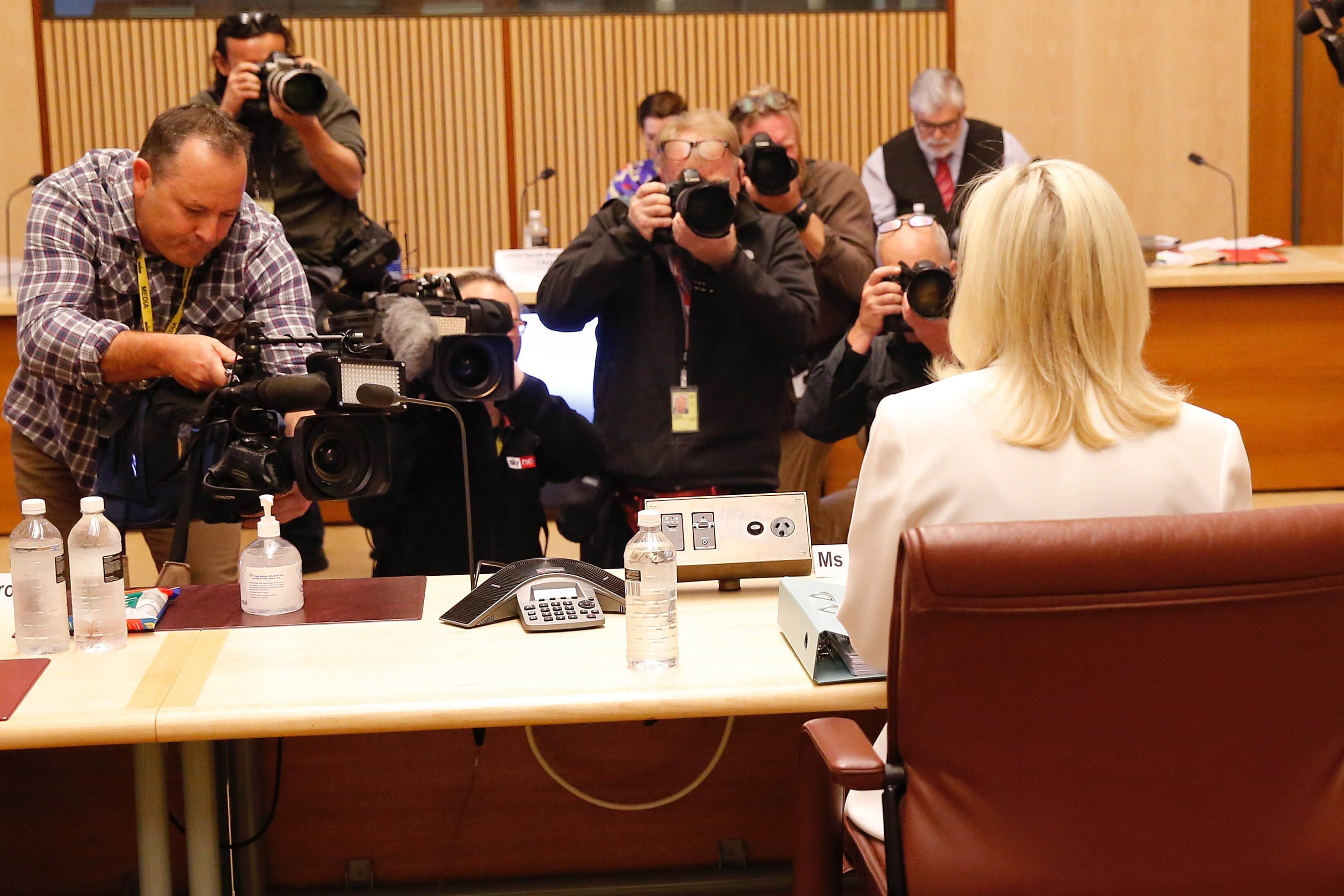 Christine Holgate, wearing white, looks ahead as photographers film her