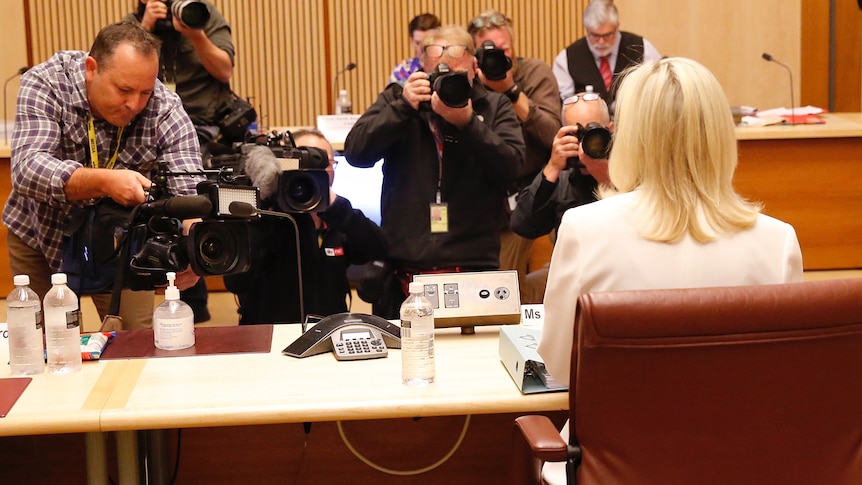 Christine Holgate, wearing white, looks ahead as photographers film her