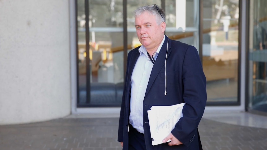 Rex Patrick, in a blue suit and no tie, walks outside the High Court, holding papers.