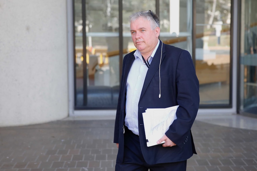 Rex Patrick, in a blue suit and no tie, walks outside the High Court, holding papers.