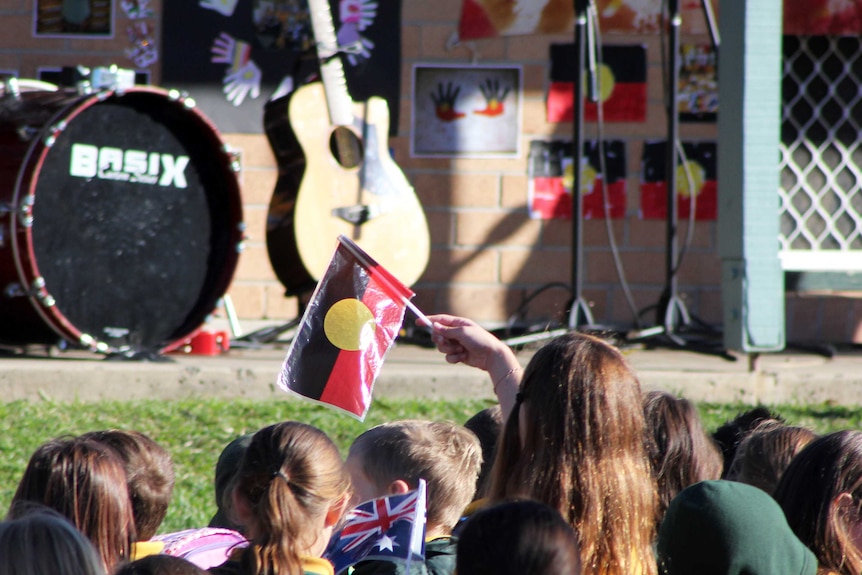 A student waves the Indigenous flag at Bellambi Public School's Reconciliation Week commemorations.