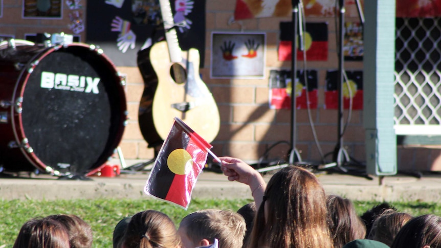 A student waves the Indigenous flag at Bellambi Public School's Reconciliation Week commemorations.