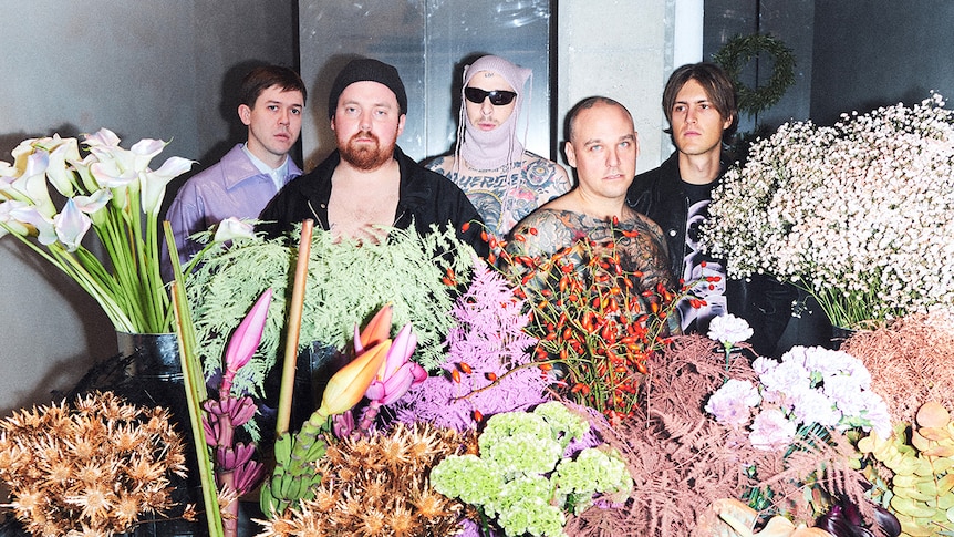 Five members of Viagra Boys stand unsmiling surrounded by large bunches of flowers.