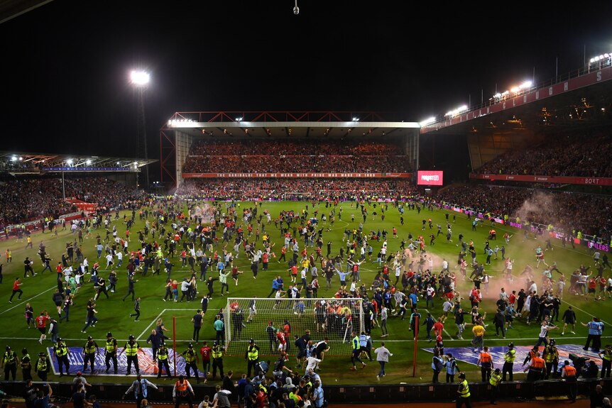Soccer fans in England run onto the field in celebration after winning an important match