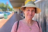 Smiling woman wearing pink shirt and beige visor, standing outside bank on footpath