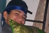 Chikayne Heslip hugging a green pillow, wearing a cap backwards.