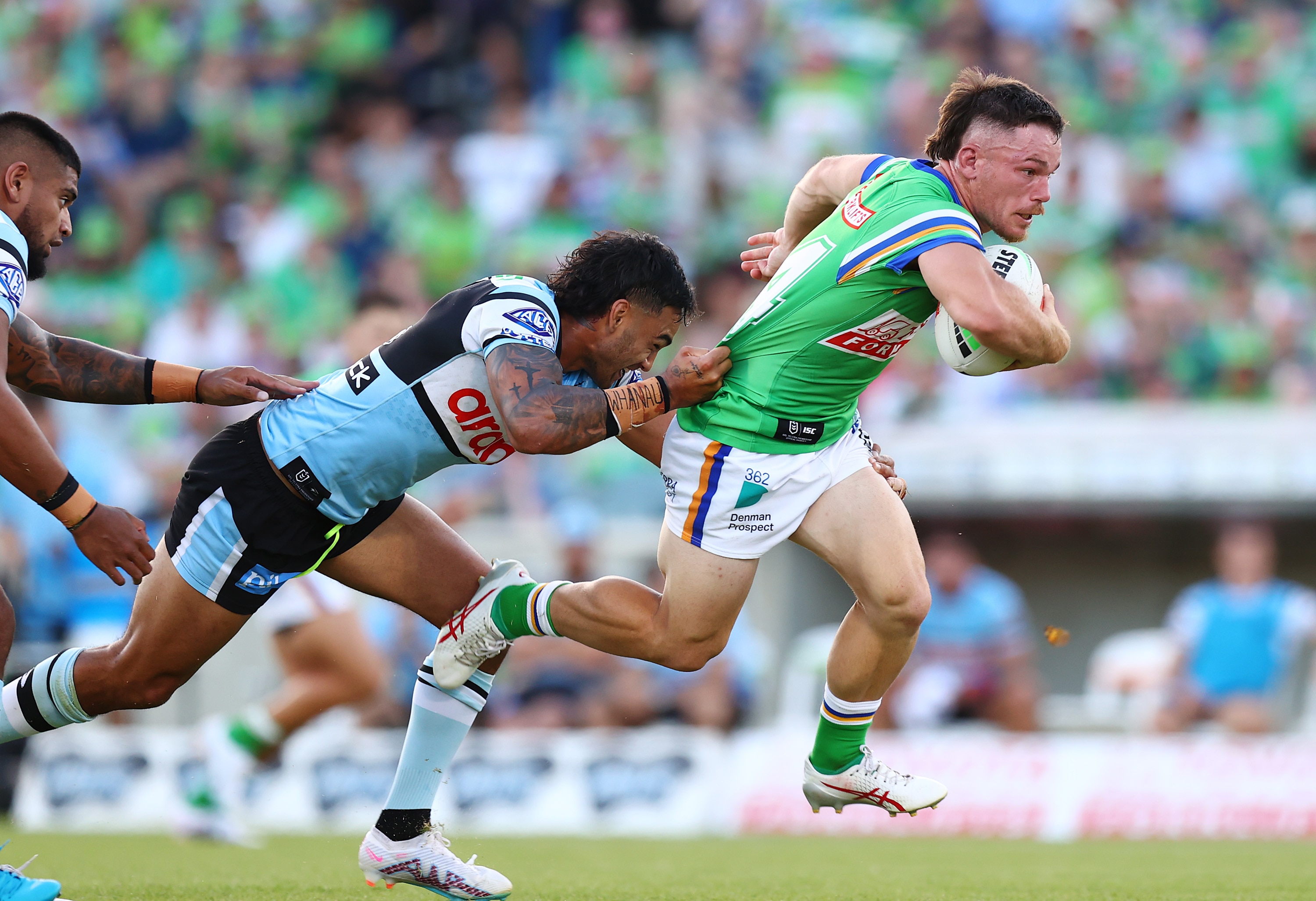 An rugby league player holding the ball runs as another player grabs his jersey from behind. 