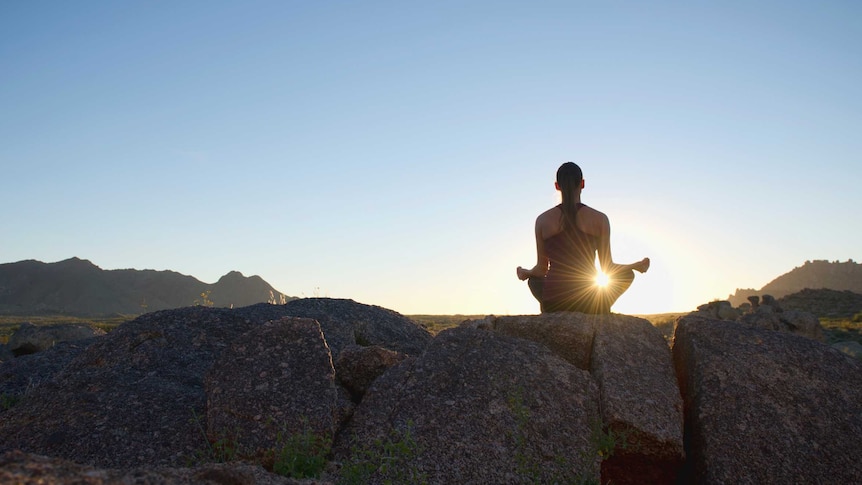 A woman meditating at sunset on a rock cliff.