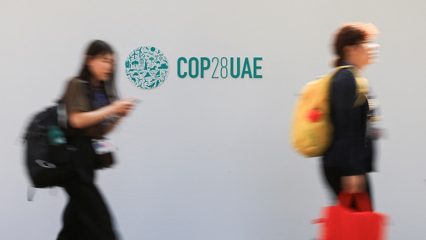 Delegates walk past a logo of the COP28 climate summit in Dubai.