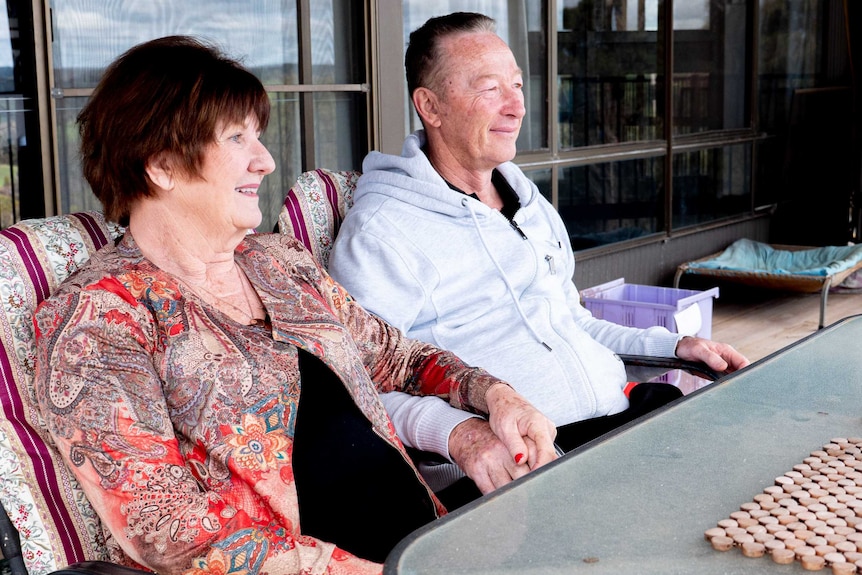 A man and a woman sitting at a table on a balcony looking off into the distance.