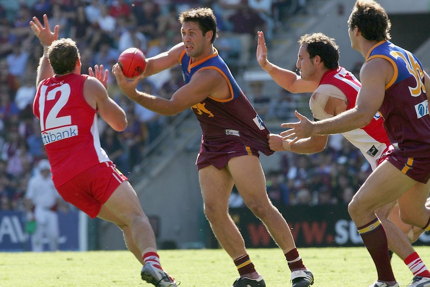 An AFL footballer looks wide-eyed as he handballs the ball while two defenders try to close him down.