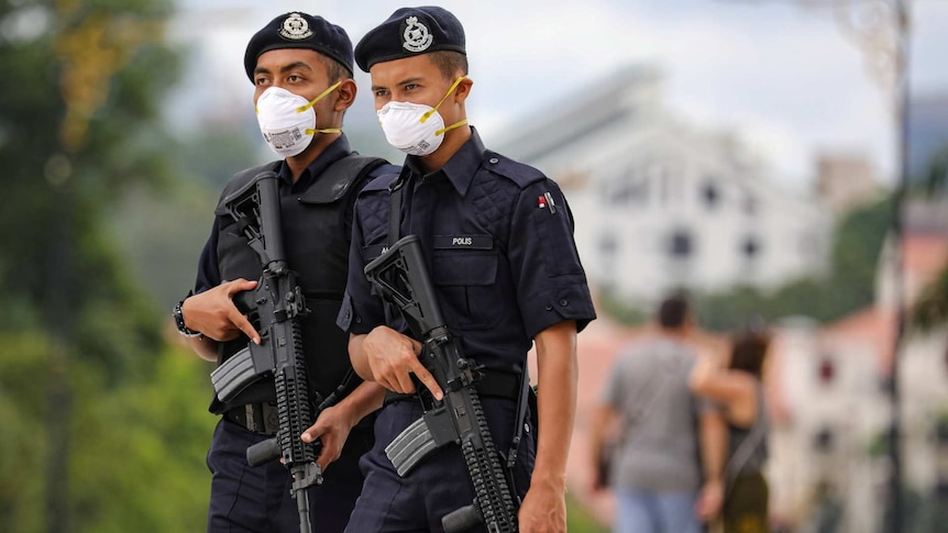 two Malaysian police officers carrying rifles and wearing face masks outside standing next to each other