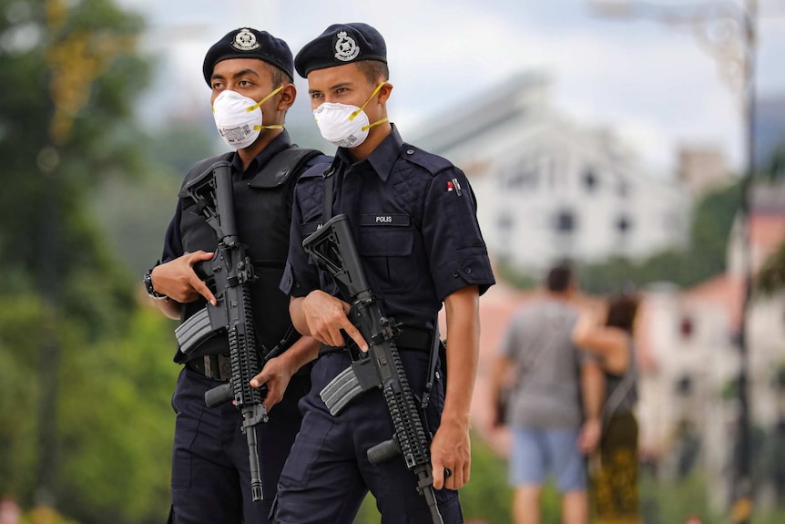 two Malaysian police officers carrying rifles and wearing face masks outside standing next to each other