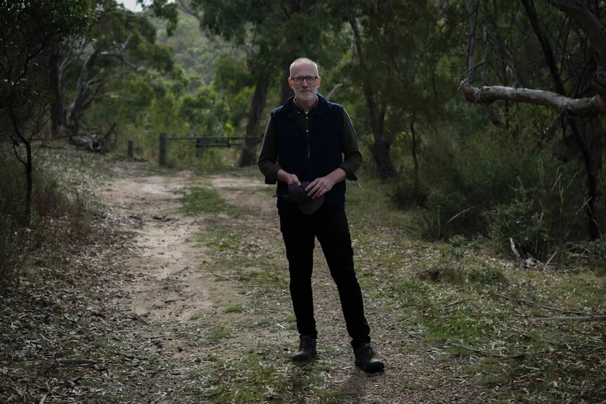 A man in dark clothing stands in front of a bush track.