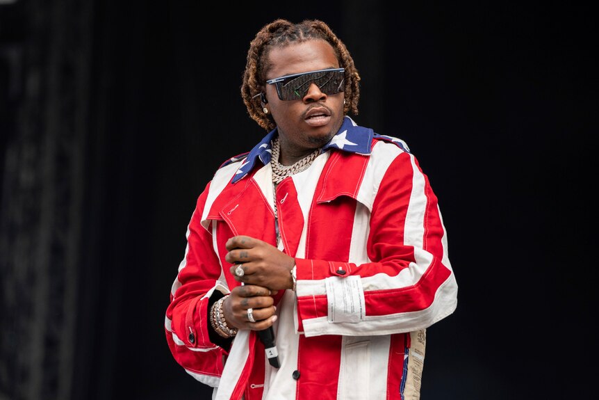 Gunna wears sunglasses and a jacket with an American flag pattern.