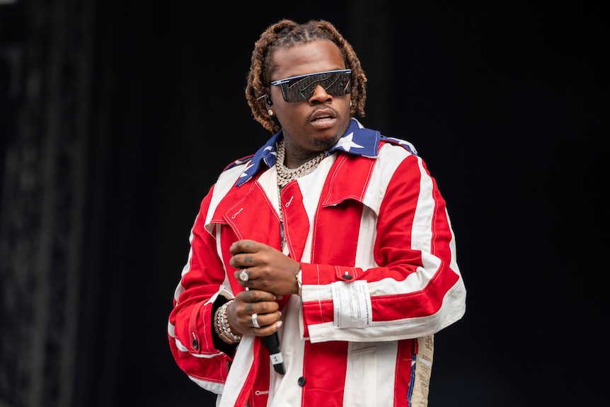 Gunna wears sunglasses and a jacket with an American flag pattern.