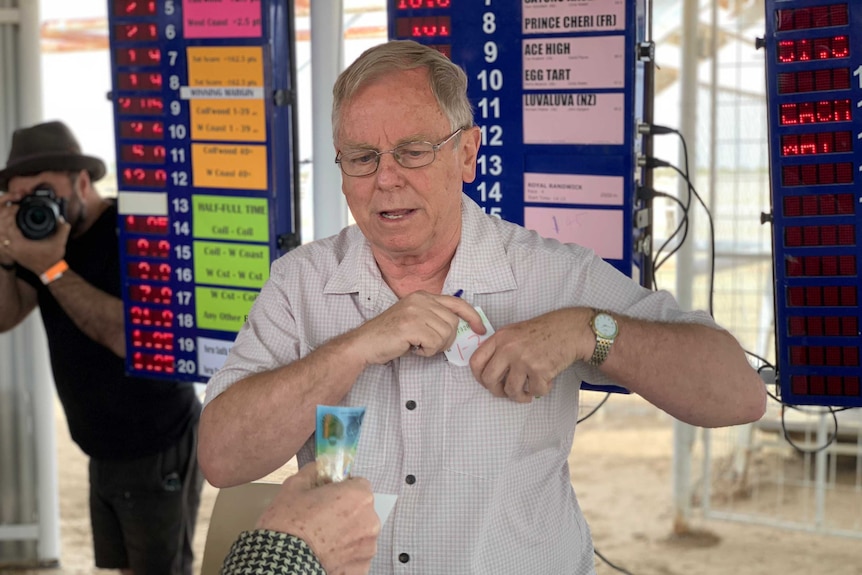 A man in a grey shirt takes bets at the races.