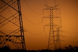 Powerlines suspended between towers against orange dusk  sky.