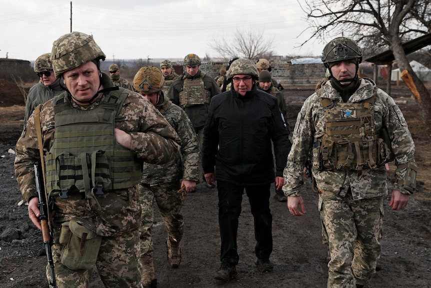 Ukrainian politician dressed in black walks alongside armed soldiers.