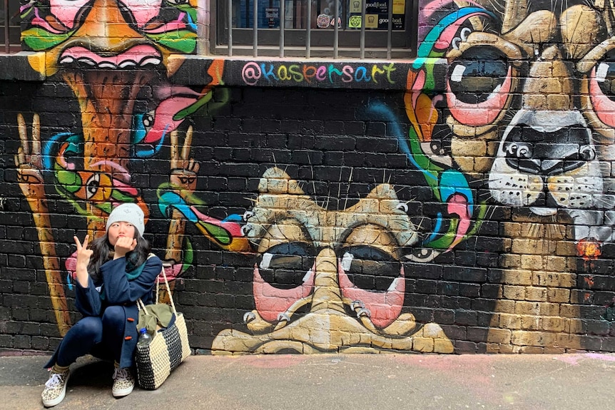 A woman poses for a photo in front of street art work.