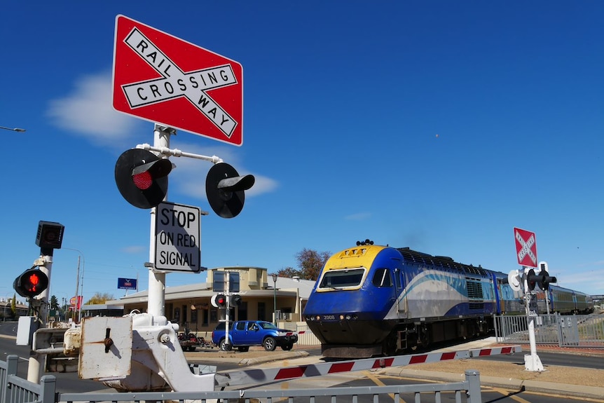 A train travels over a road with boom gates and flashing lights to warn drivers.