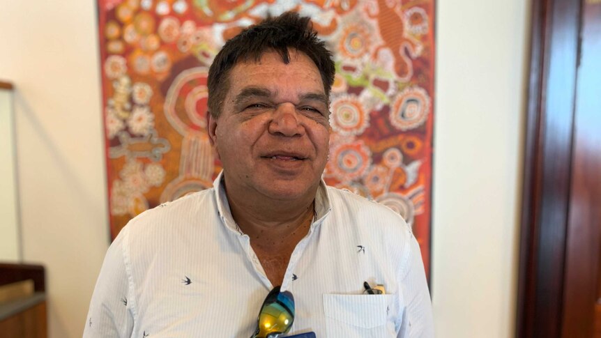 A smiling man looking into the camera with Aboriginal art in the background