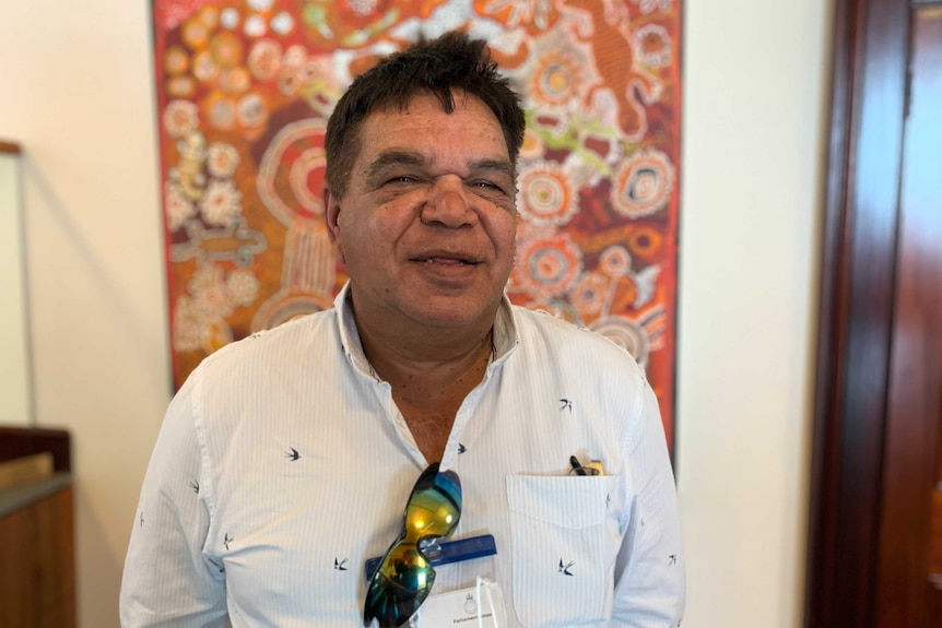 A smiling man looking into the camera with Aboriginal art in the background