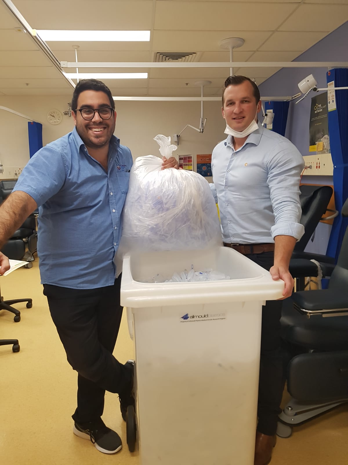 Two men hold a bag of syringe caps.