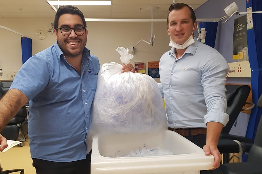 Two men hold a bag of syringe caps.