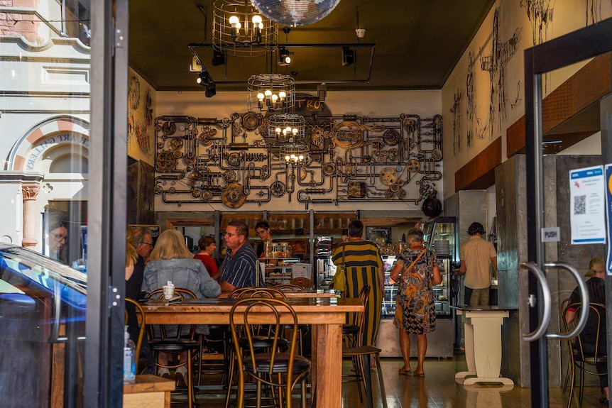The interior of a cafe with wooden tables and chairs and intricate lightshades and wall decor.