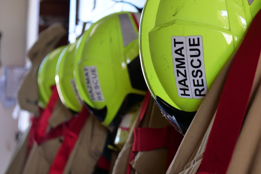 A row of fire fighting helmets and jackets hanging up at a station.