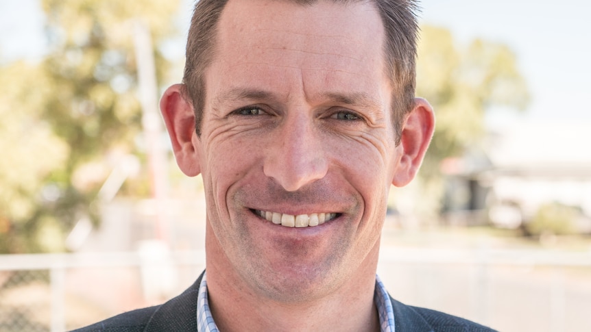 A smiling man in a blazer and shirt in outback Queensland.