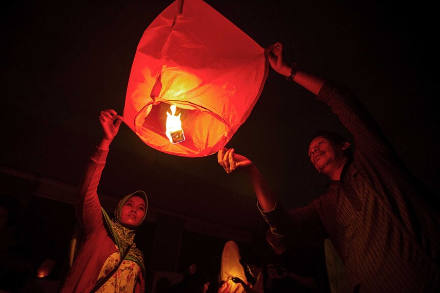 A man and a woman hold a lantern containing a candle at night.