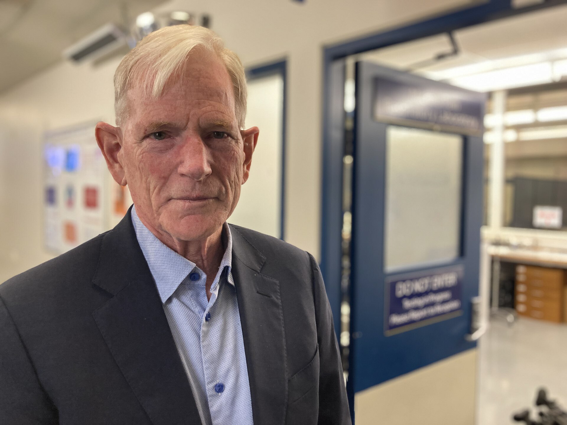 A man looking at the camera with a hospital behind him
