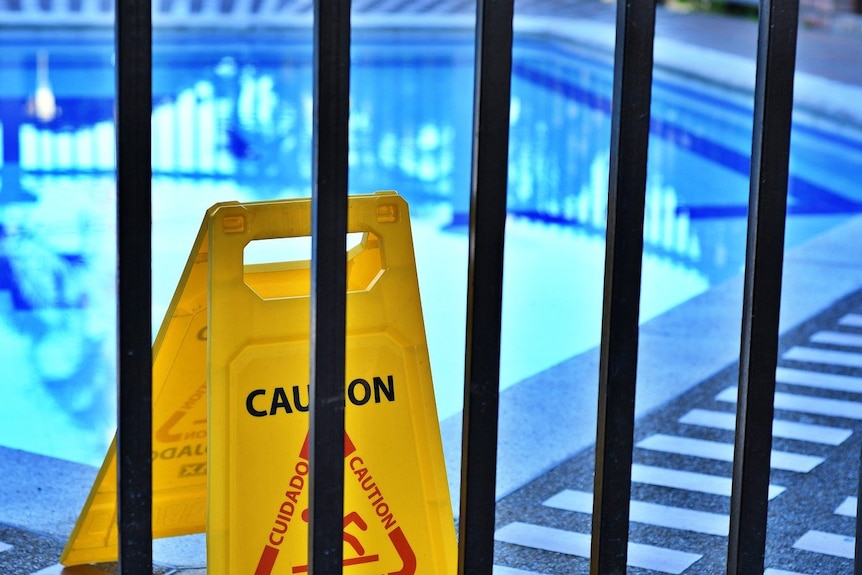 A sign that says "caution" next to a swimming pool.