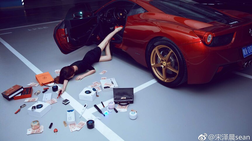 A woman falls out of a red sports car with make up and cash scattered around her.