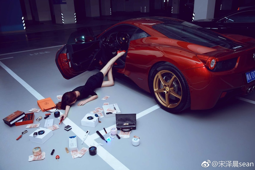 A woman falls out of a red sports car with make up and cash scattered around her.