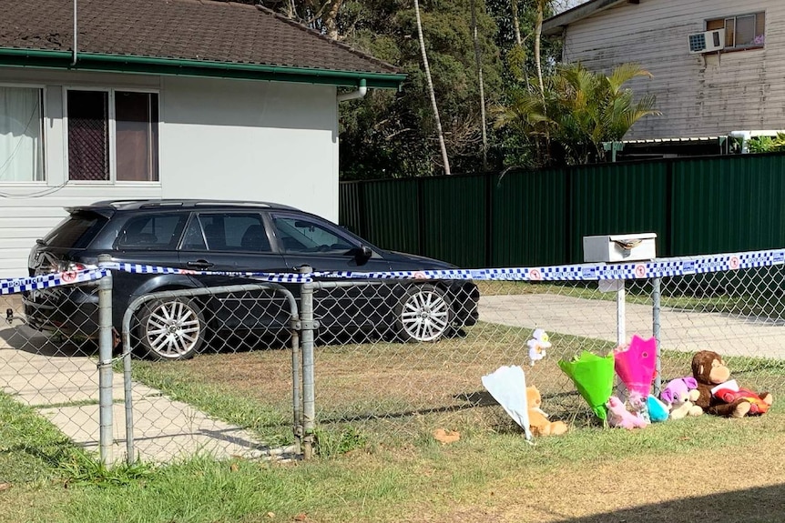 Bunches of flowers lean against a wire fence that borders the green one-storey home where the girls died.