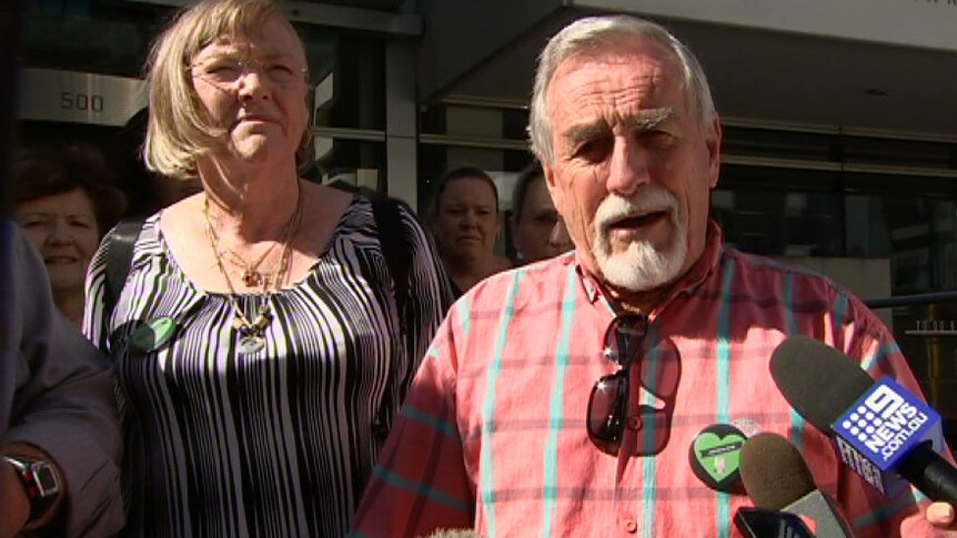 A man reads from a statement while standing alongside a woman outside Perth District Court, with a microphone in front of him.