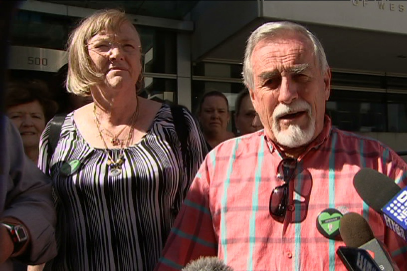 A man reads from a statement while standing alongside a woman outside Perth District Court, with a microphone in front of him.