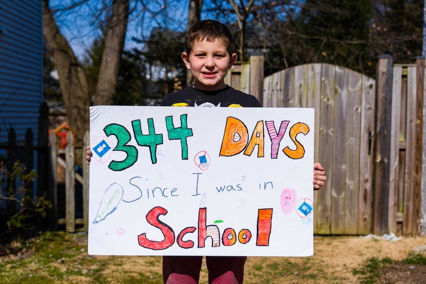 A little boy holding a sign reading '344 days since I was in school'
