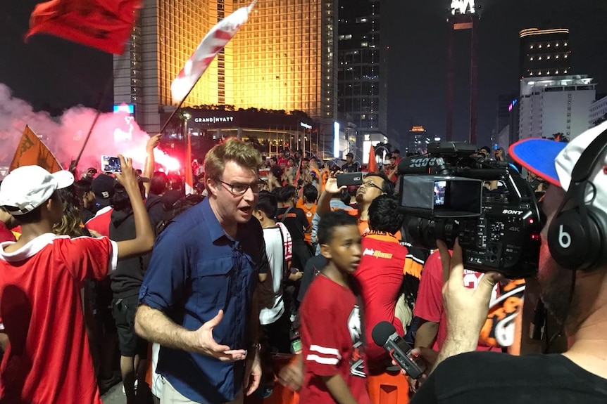 David Lipson shoots a piece to camera among a crowd of rowdy soccer fans.