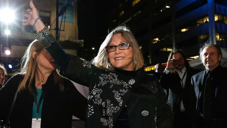 Carrie Fisher waves as people take photos.