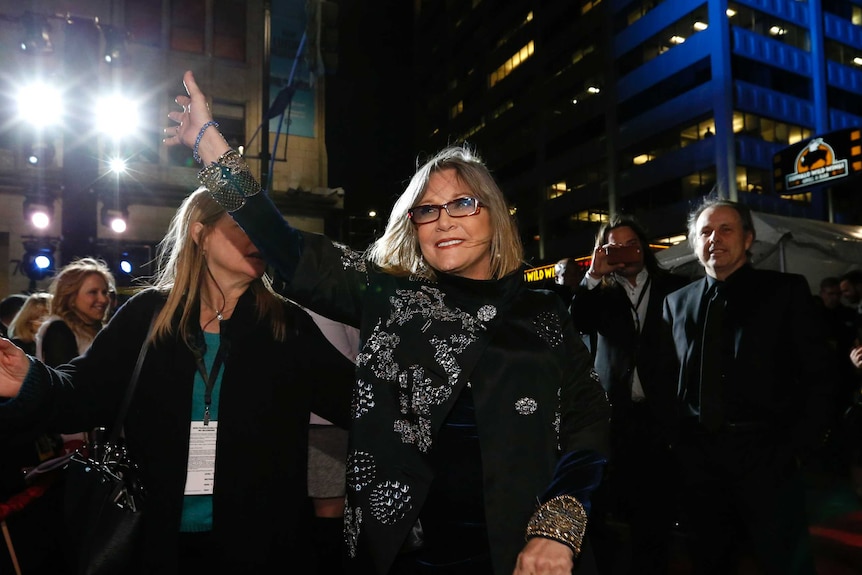 Carrie Fisher waves as people take photos.