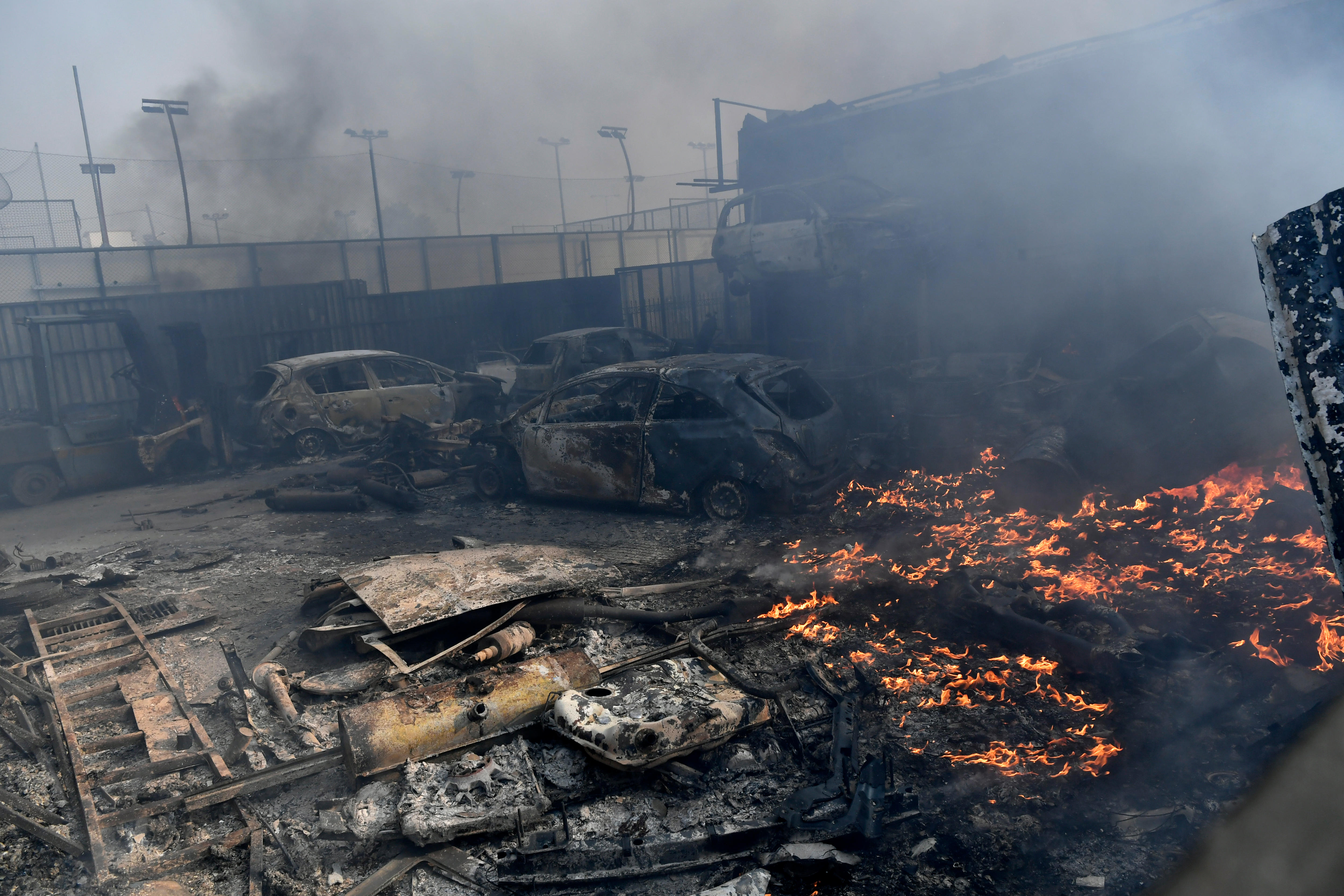 Flames burn next to three blackened cars in a carpark.